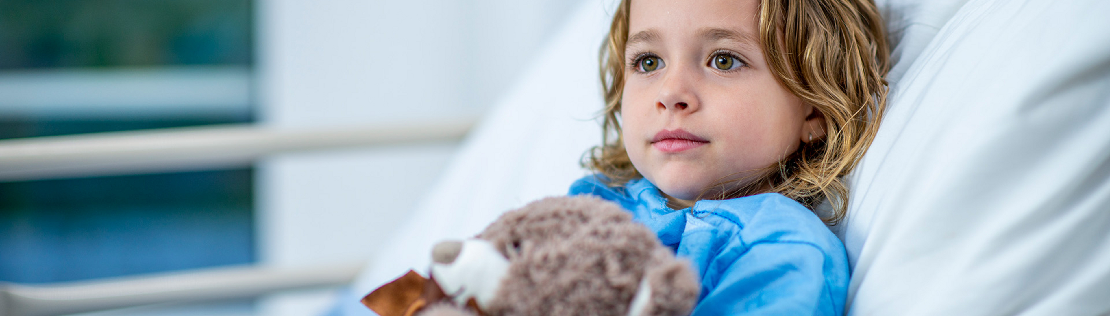 Kind im Krankenhausbett mit Teddybär