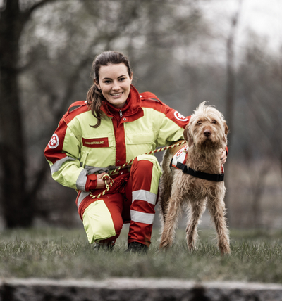 Eine Rettungskraft in rot-gelber Kleidung posiert mit einem Hund.