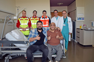 Rajko Nikolic und sein Sohn sitzen gemeinsam im Krankenhaus, hinter ihnen stehen drei Sanitäter und zwei Ärzte.